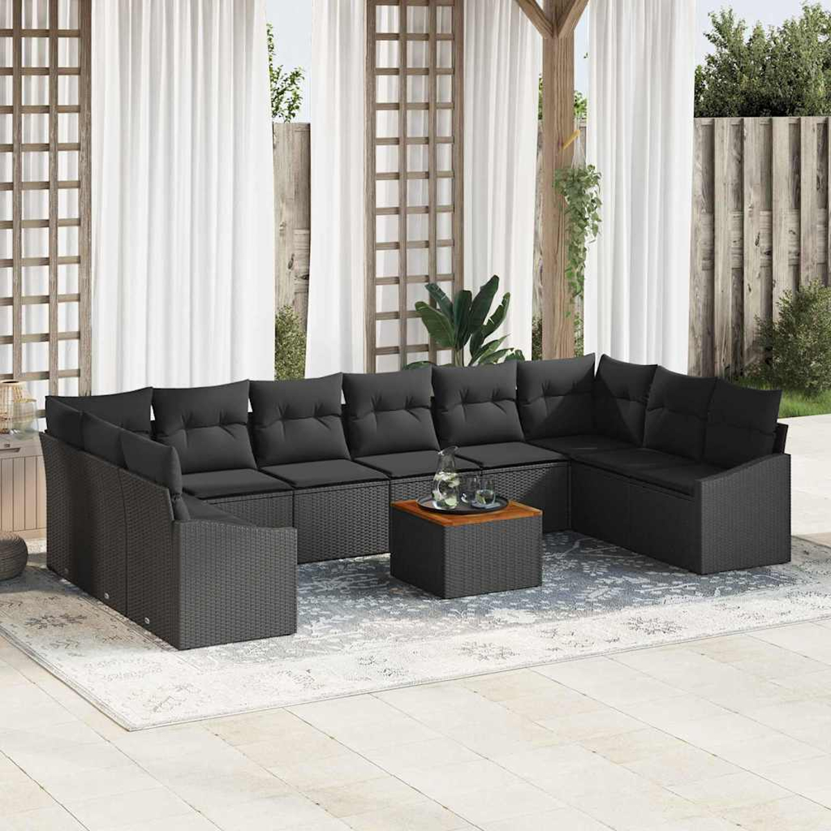 Outdoor-Ecksofa mit schwarzen Kissen. Davor steht ein kleiner quadratischer Tisch mit Getränken. Weiße Vorhänge und Holzgitter im Hintergrund.