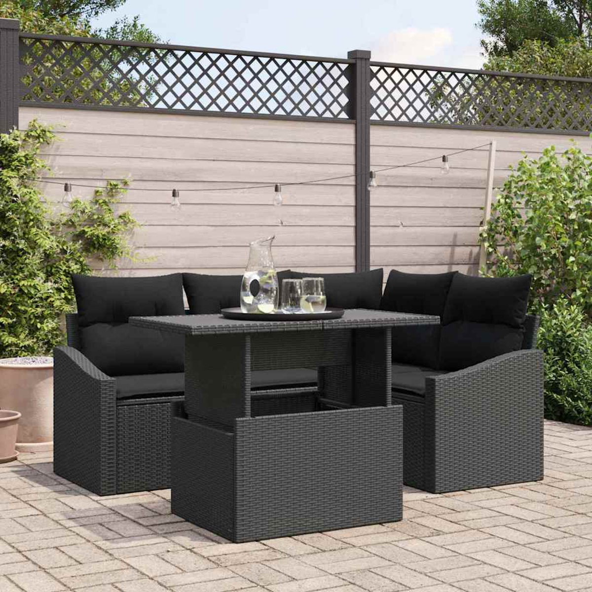 Garten-Terrassenset mit schwarzen Kissen, einem Tisch mit Getränken und einem Holzzaun im Hintergrund.