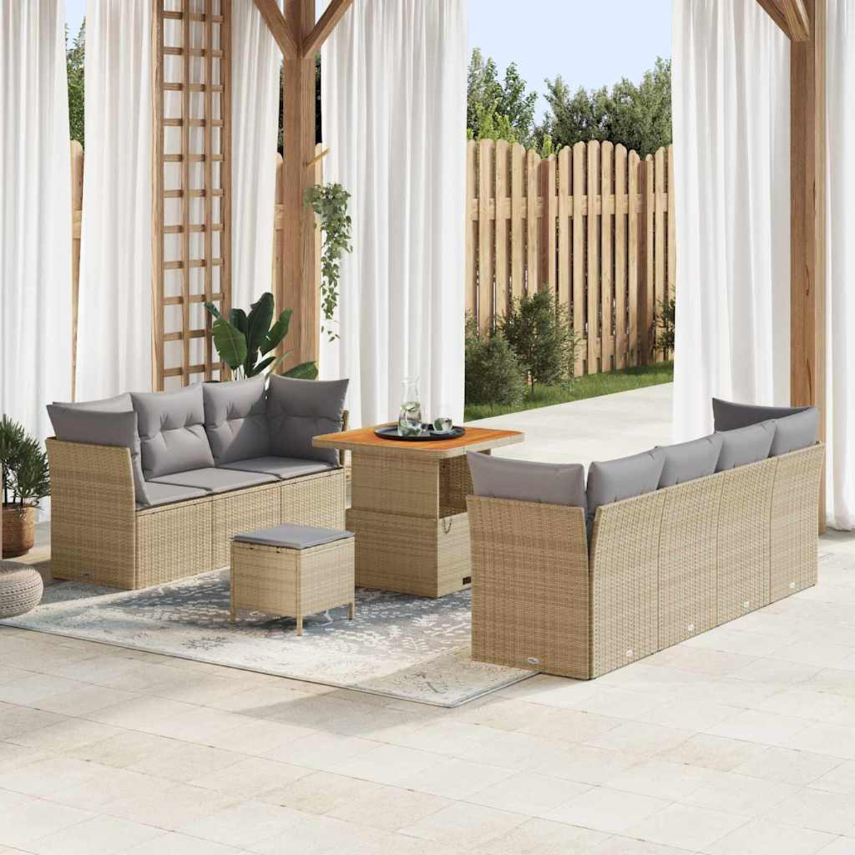 Set da patio esterno con divani intrecciati, cuscini grigi, un tavolino e un pouf. Tende bianche e una staccionata in legno sullo sfondo.