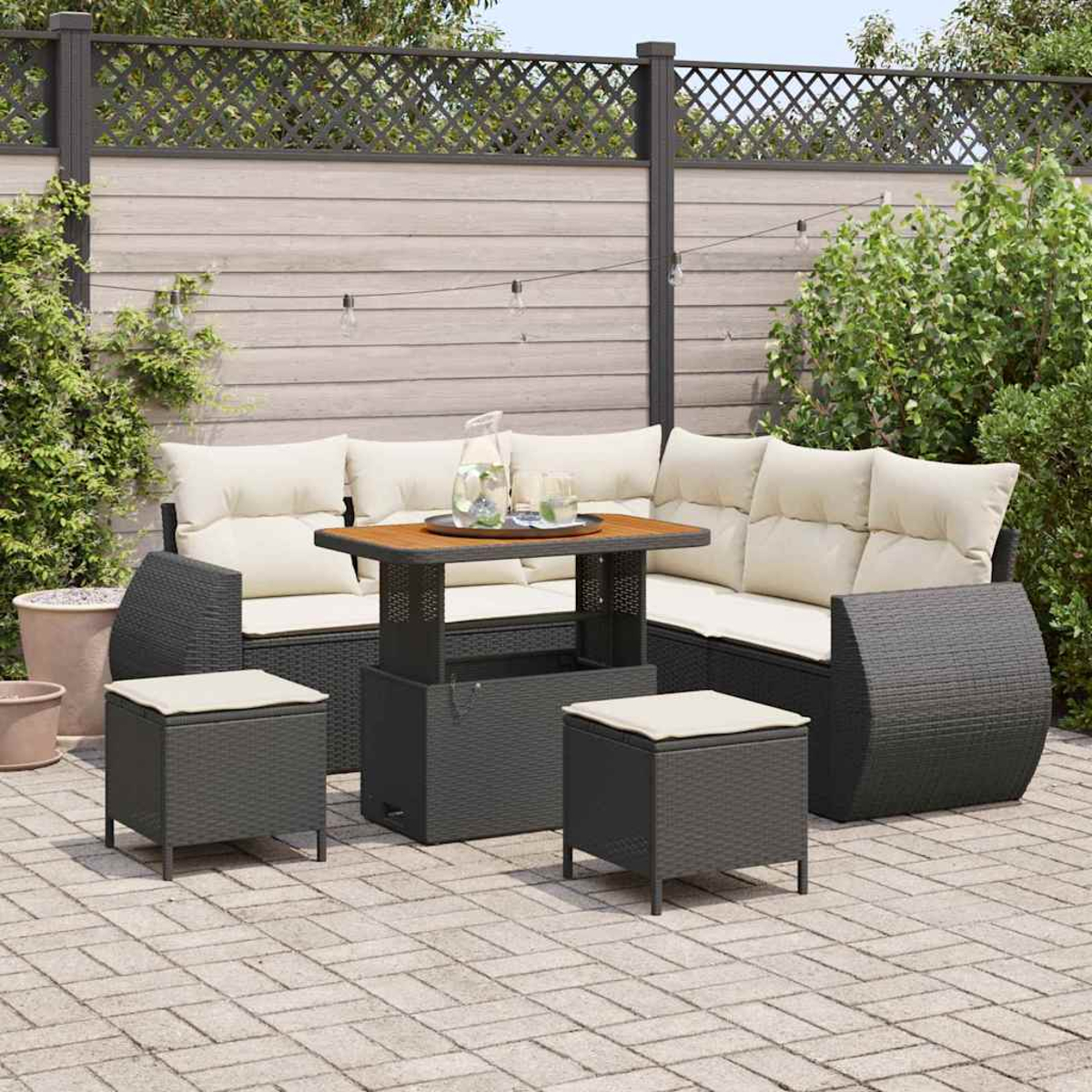 Garten-Sitzgruppe mit Sofa, zwei Hockern und einem Tisch. Das Set befindet sich auf einer Ziegelterrasse mit Zaun und Grün im Hintergrund.