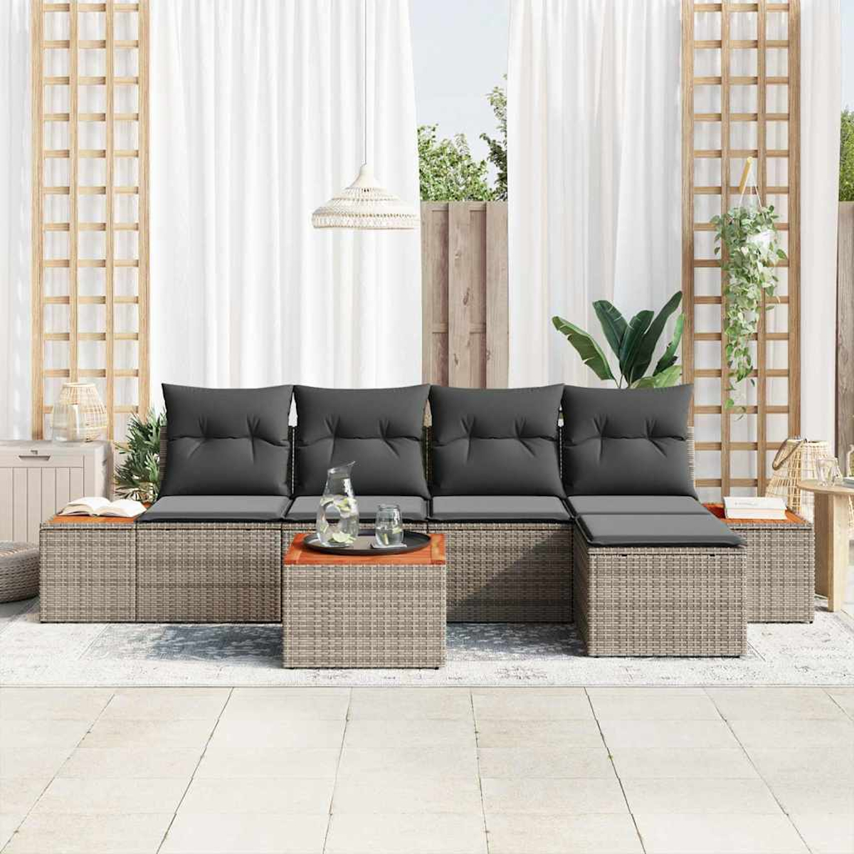 Gartenmöbelset mit grauen Kissen. Enthält Sofa, Ottomane und Couchtisch. Weiße Vorhänge und Holzgitter im Hintergrund.