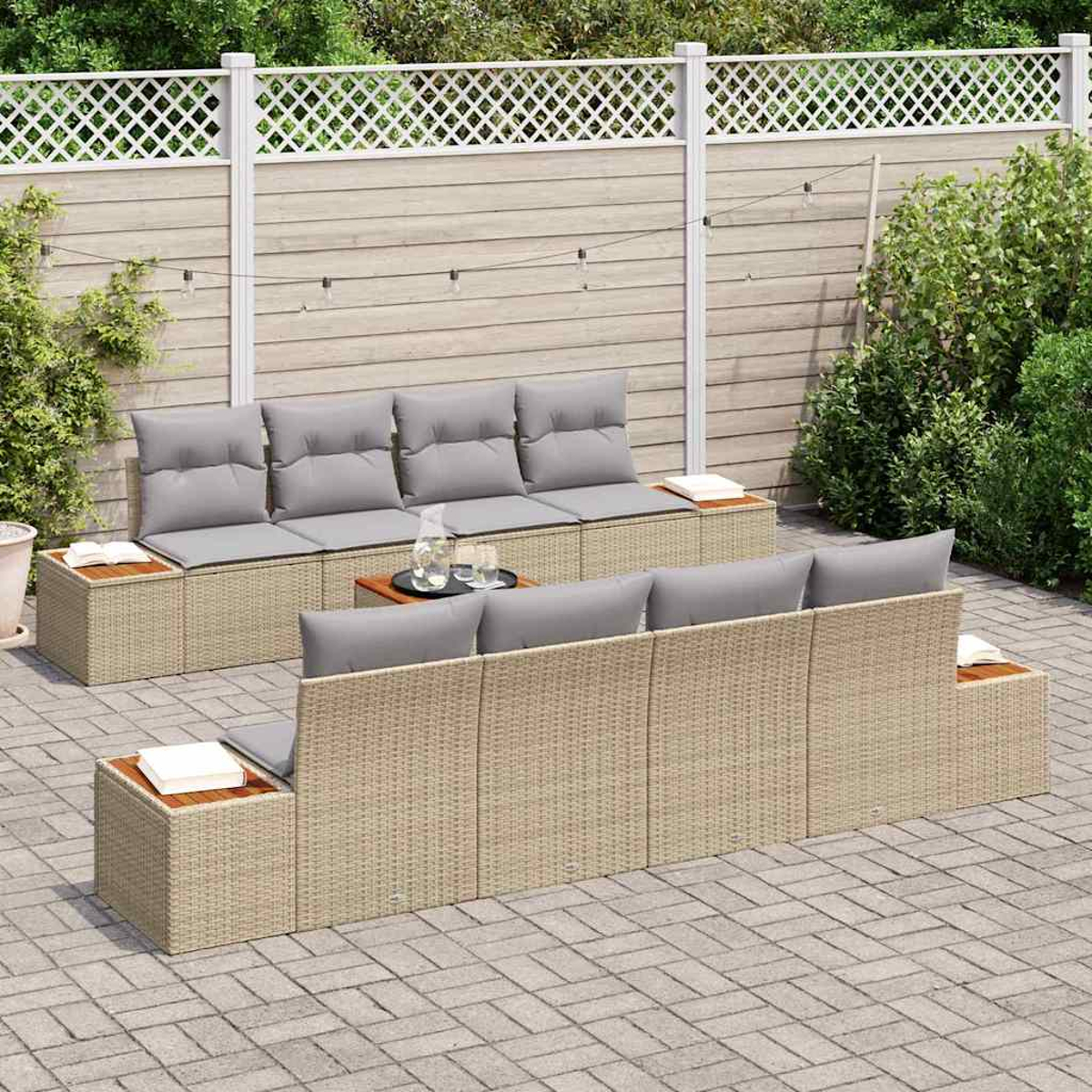 Gartenmöbel-Set mit grauen Kissen. Hintergrund: Zaun, Büsche und eine Ziegelterrasse mit Lichterketten.