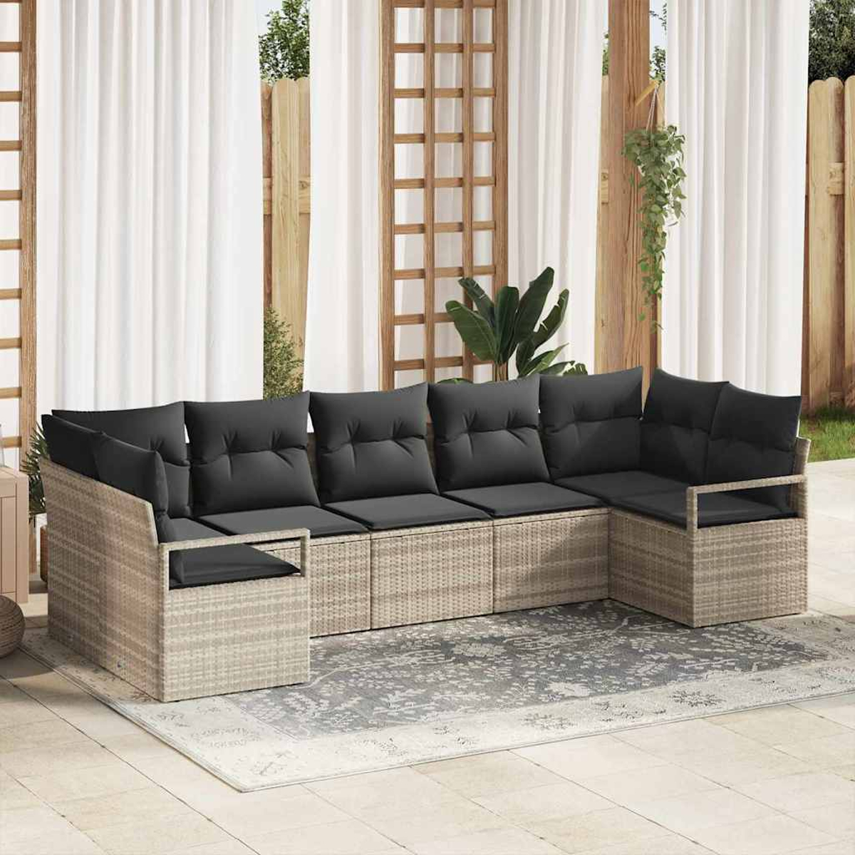 Outdoor-Ecksofa mit grauen Kissen auf einem gemusterten Teppich. Weiße Vorhänge und Holzstrukturen im Hintergrund.