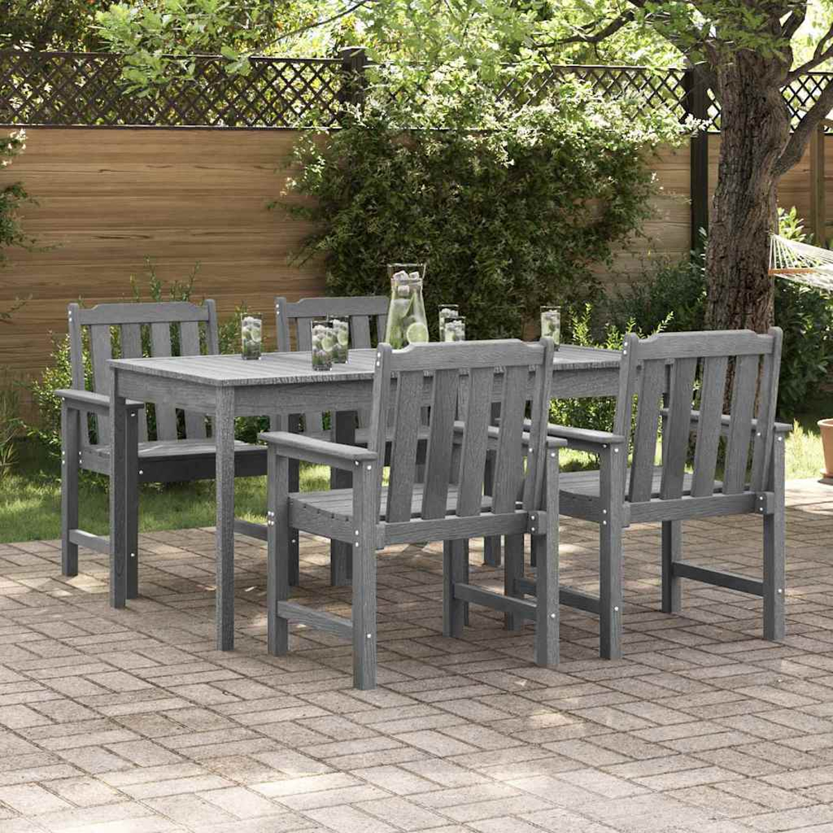 Graues Ess-Set aus Holz im Freien auf einer Ziegelstein-Terrasse. Tisch mit Stühlen, Getränken und üppigem Grün im Hintergrund.