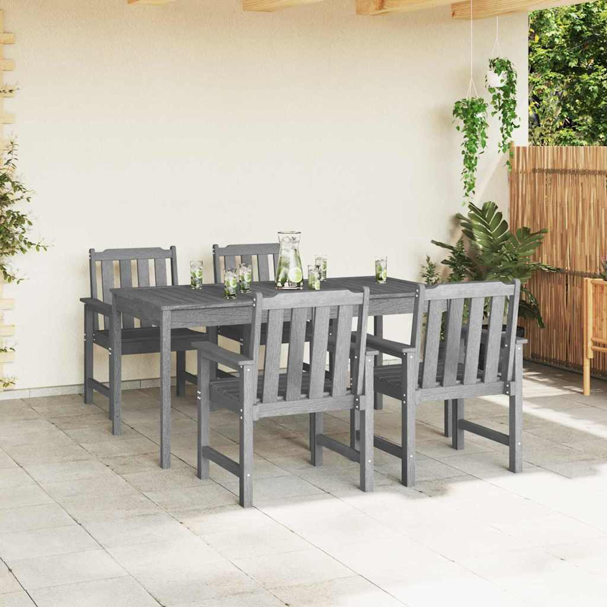 Ein graues Holz-Terrassenset mit einem rechteckigen Tisch und sechs Stühlen. Auf dem Tisch stehen ein Krug und Gläser. Pflanzen und ein Bambuszaun sind im Hintergrund.