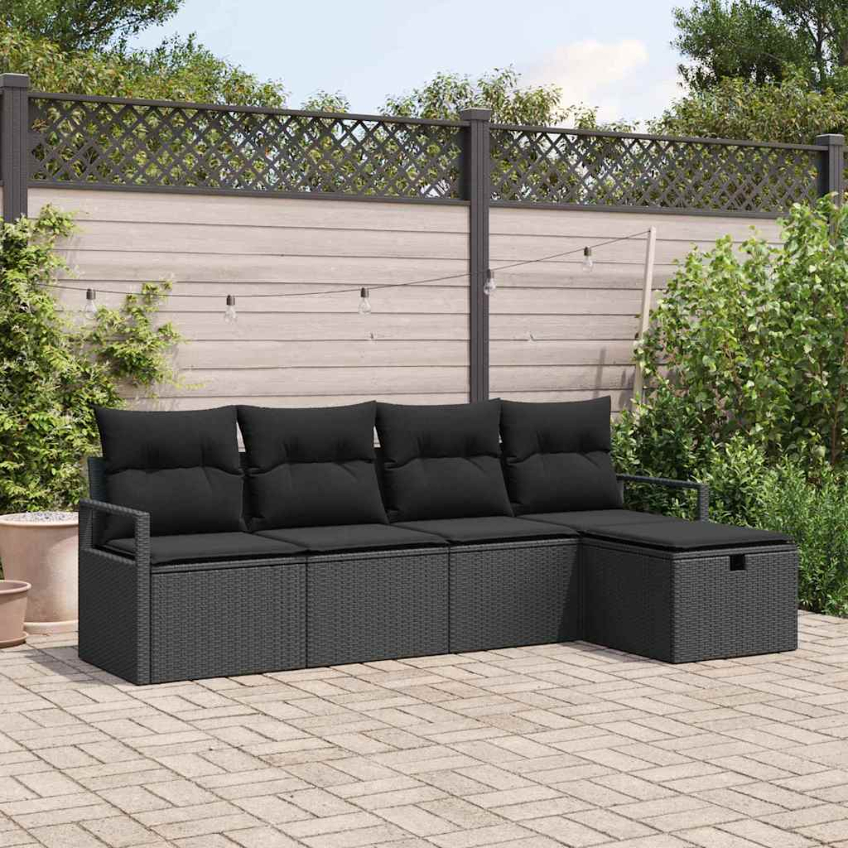 Ein dunkelgraues Korbsessel-Sofa mit schwarzen Kissen steht auf einer Steinterrasse. Dahinter sind ein Holzzaun und Laub.