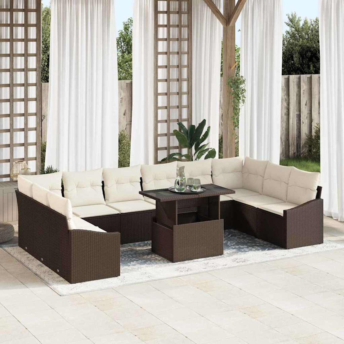 Garten-Lounge-Set mit braun gewebtem Rahmen, cremefarbenen Kissen. Mitteltisch. Weiße Vorhänge, Holzgitter und Grün im Hintergrund.