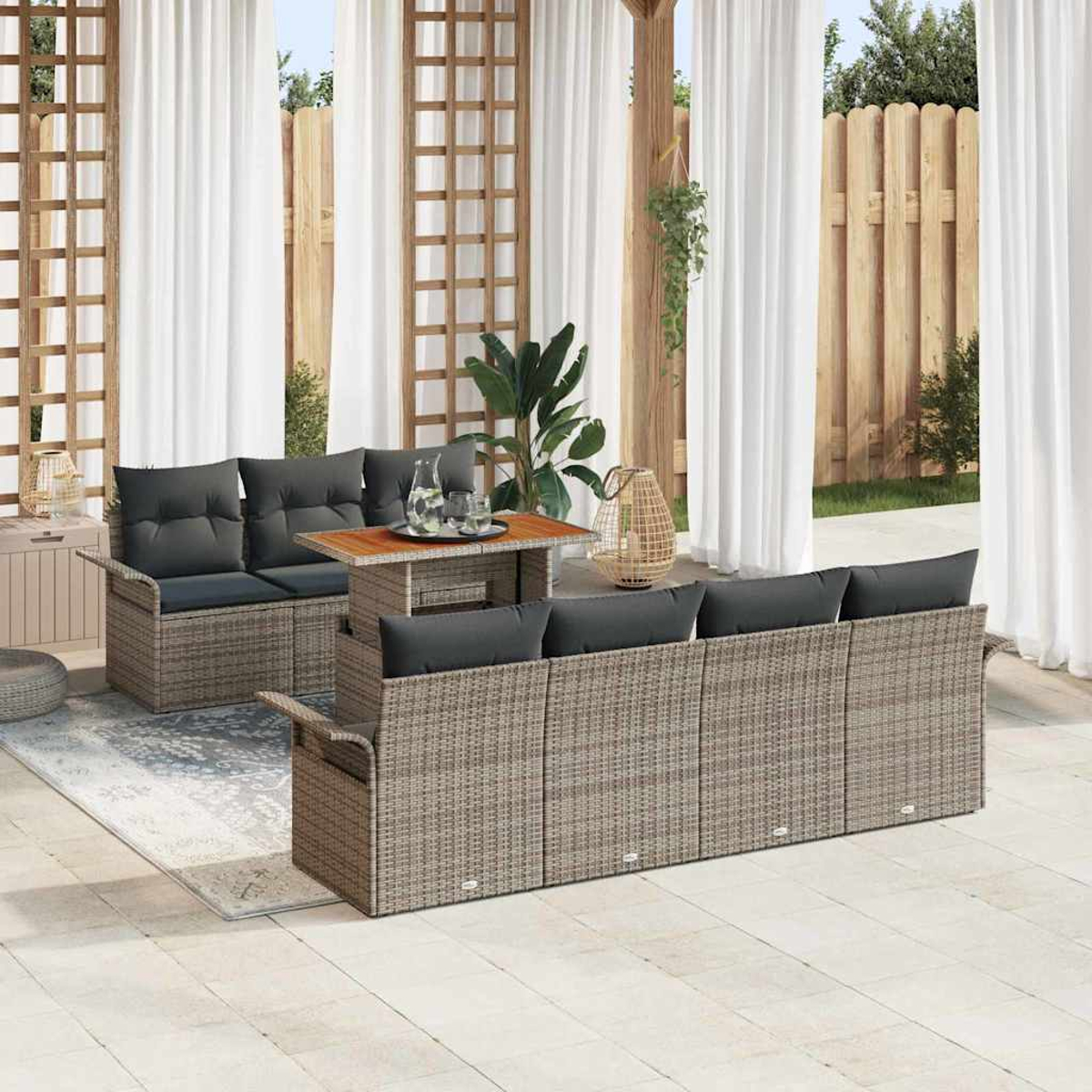 Terrassenmöbel-Set mit grauen Kissen, einem Holztisch und weißen Vorhängen. Korbmöbel auf Fliesenboden mit Zaun im Hintergrund.