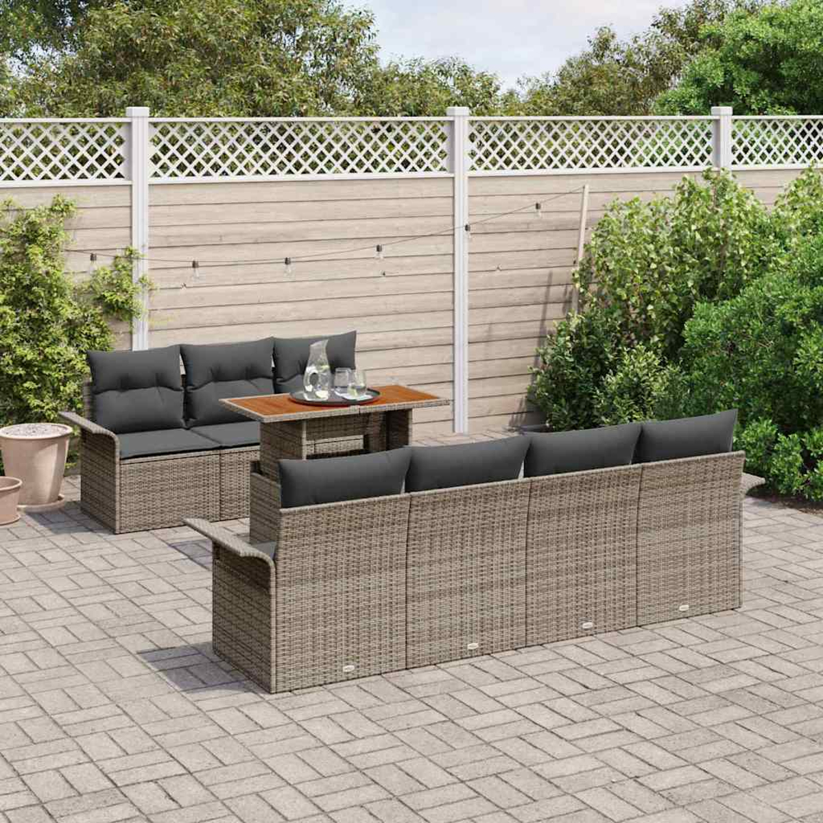 Szene im Freien mit Rattan-Möbeln. Ein Sofa, ein Liebessitz und ein Tisch mit Getränken. Hinter einem Holzzaun mit Grün.