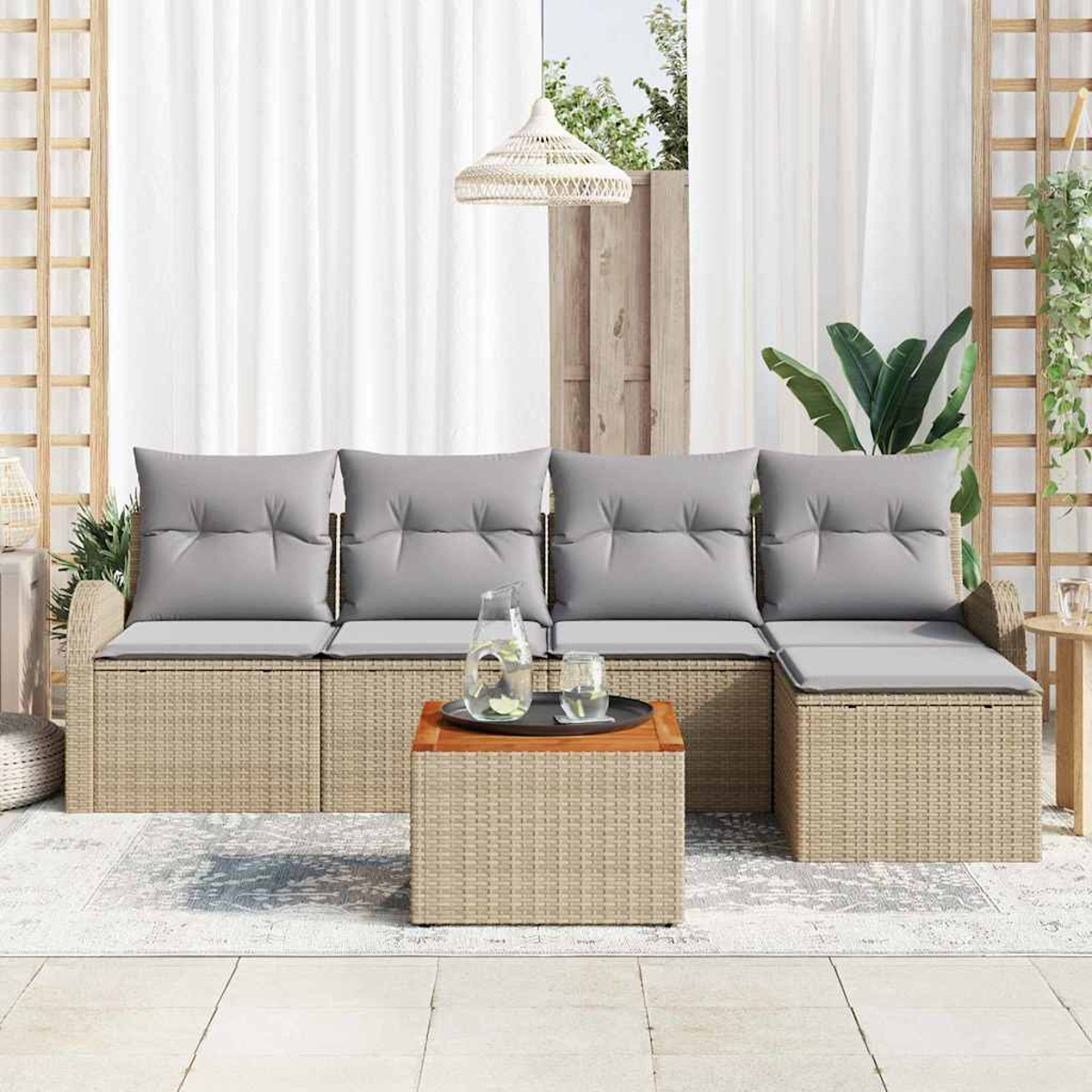 Outdoor-Korbsessel mit grauen Kissen und einem Couchtisch aus Holz. Weiße Vorhänge und eine gewebte Leuchte hängen im Hintergrund.