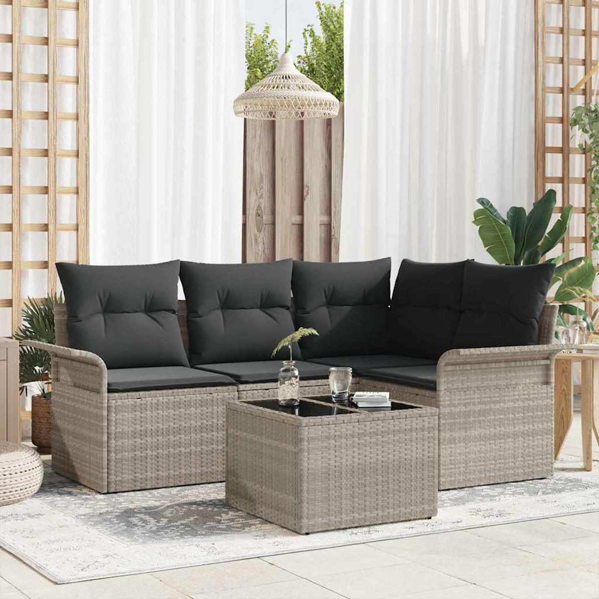 Outdoor-Terrassenset: graues Korbmöbelsofa mit schwarzen Kissen, Couchtisch mit Glasplatte, Teppich und weißen Vorhängen.