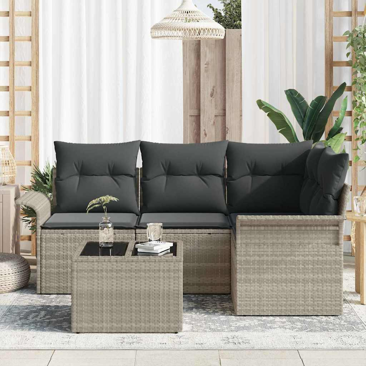 Outdoor-Sitzgruppe mit grauen Kissen, einem Couchtisch und einer gewebten Lampe. Weiße Vorhänge und Grün im Hintergrund.