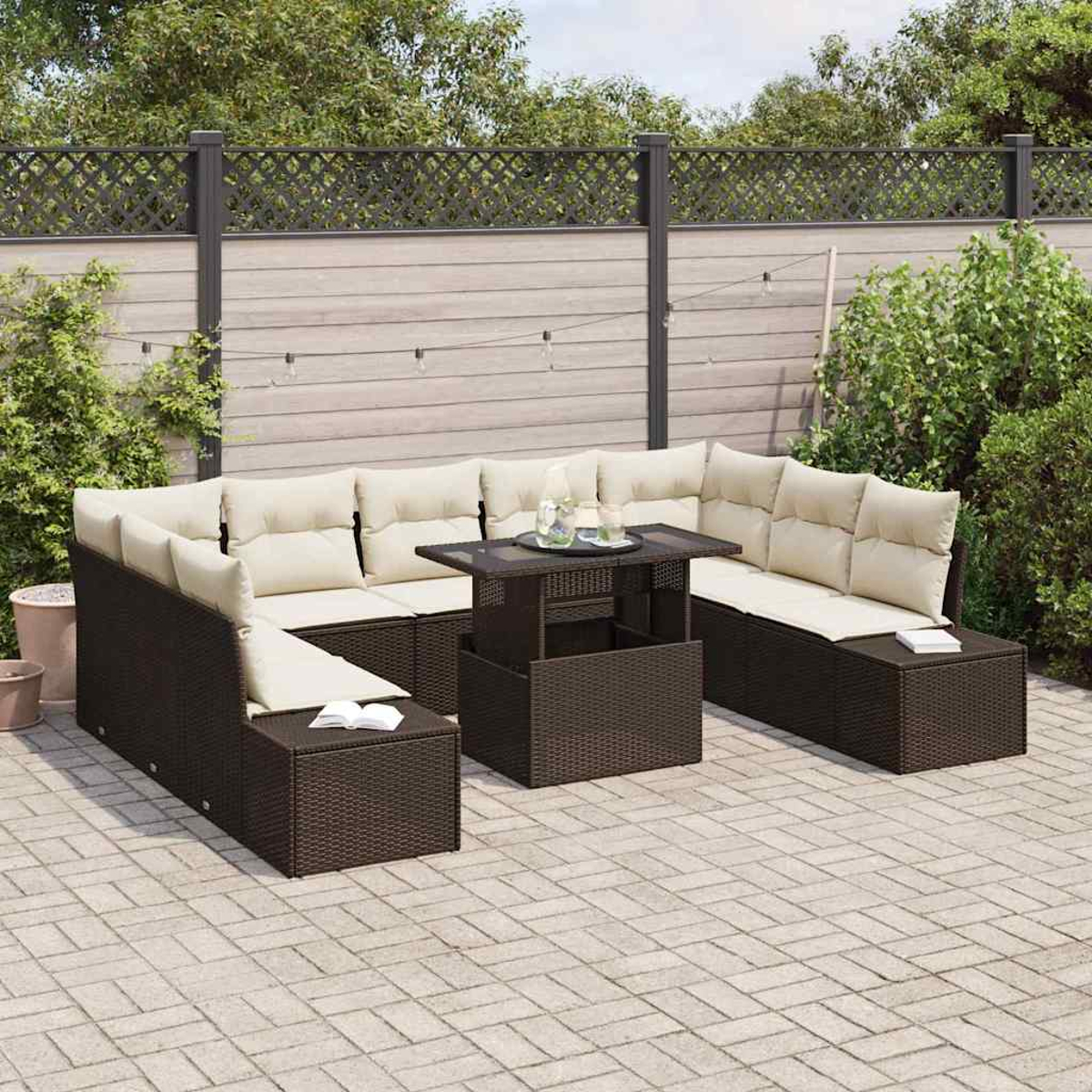 Garten-Terrassenset mit braunen Korbmöbeln und beigen Kissen. Ein Tisch mit Glasplatte steht in der Mitte. Im Hintergrund sind ein Zaun und Bäume zu sehen.