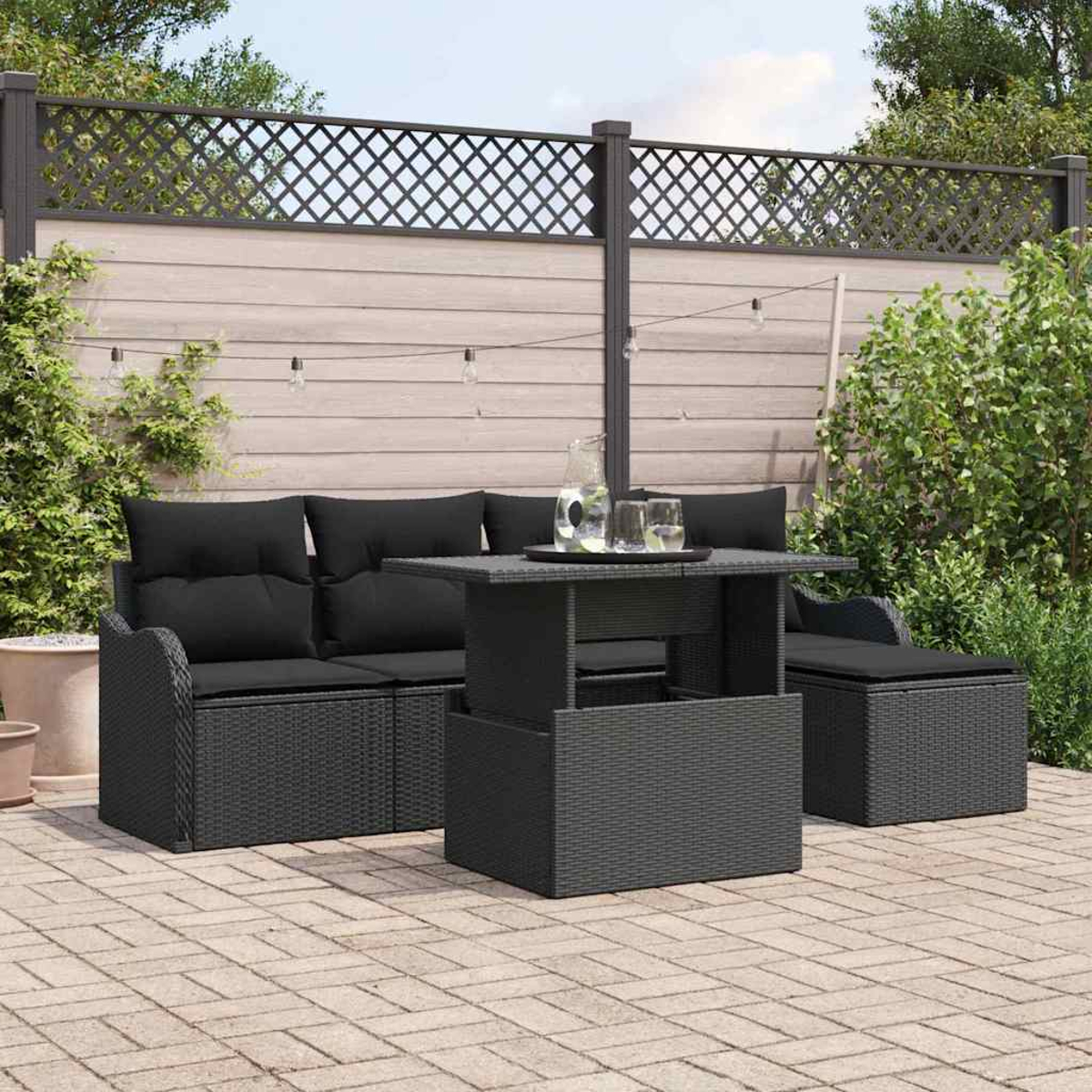 Terrassenset mit schwarzen Kissen und Tisch. Hintergrund: Zaun, Pflanzen und Lichterkette.