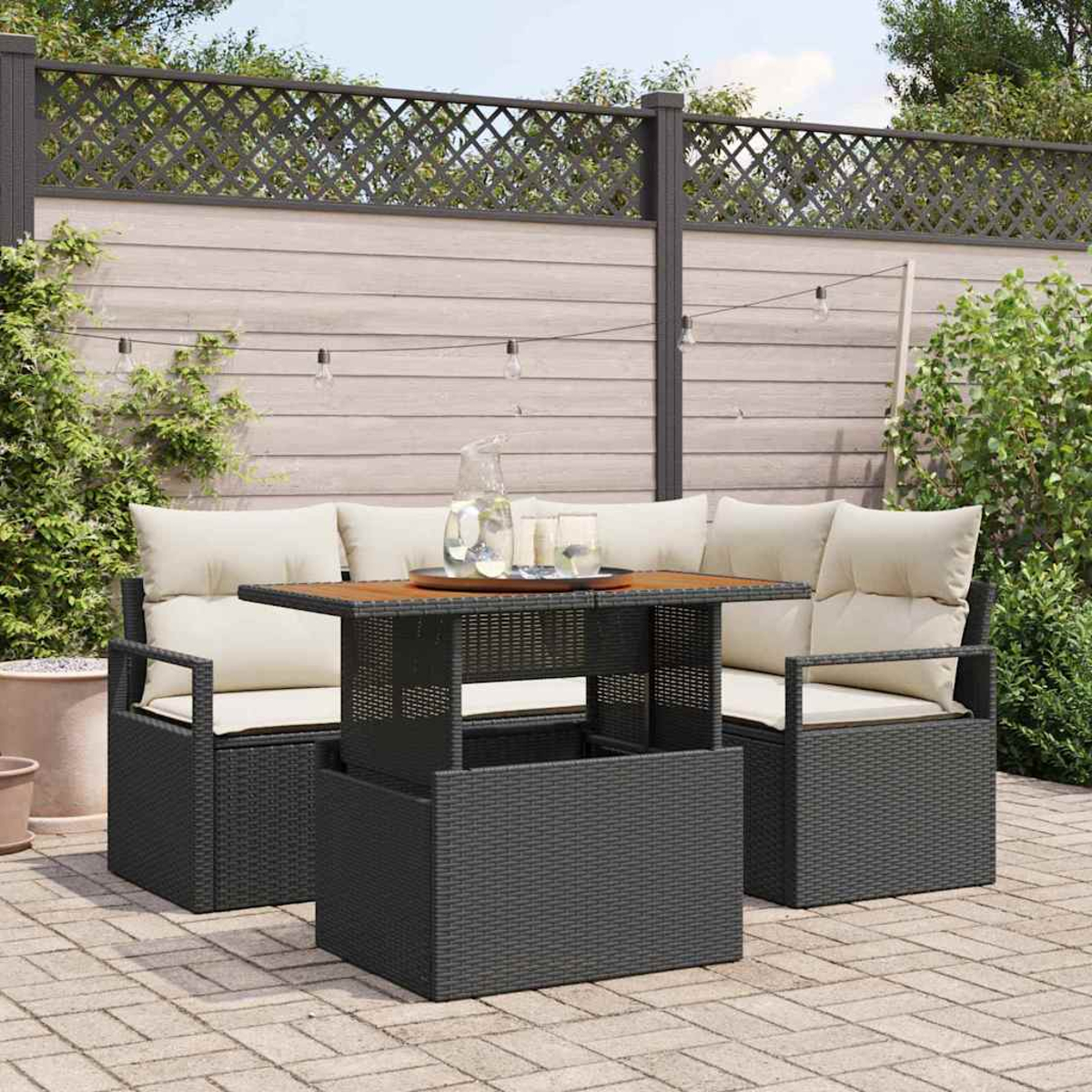 Garten-Sitzgruppe mit Tisch, Kissen und dekorativem Zaun im Hintergrund. Getränke stehen auf dem Tisch.