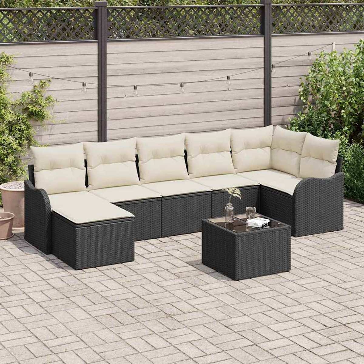 Outdoor-Ecksofa mit cremefarbenen Kissen und einem kleinen Tisch auf einer Ziegelterrasse. Dahinter ein Zaun und Grün.