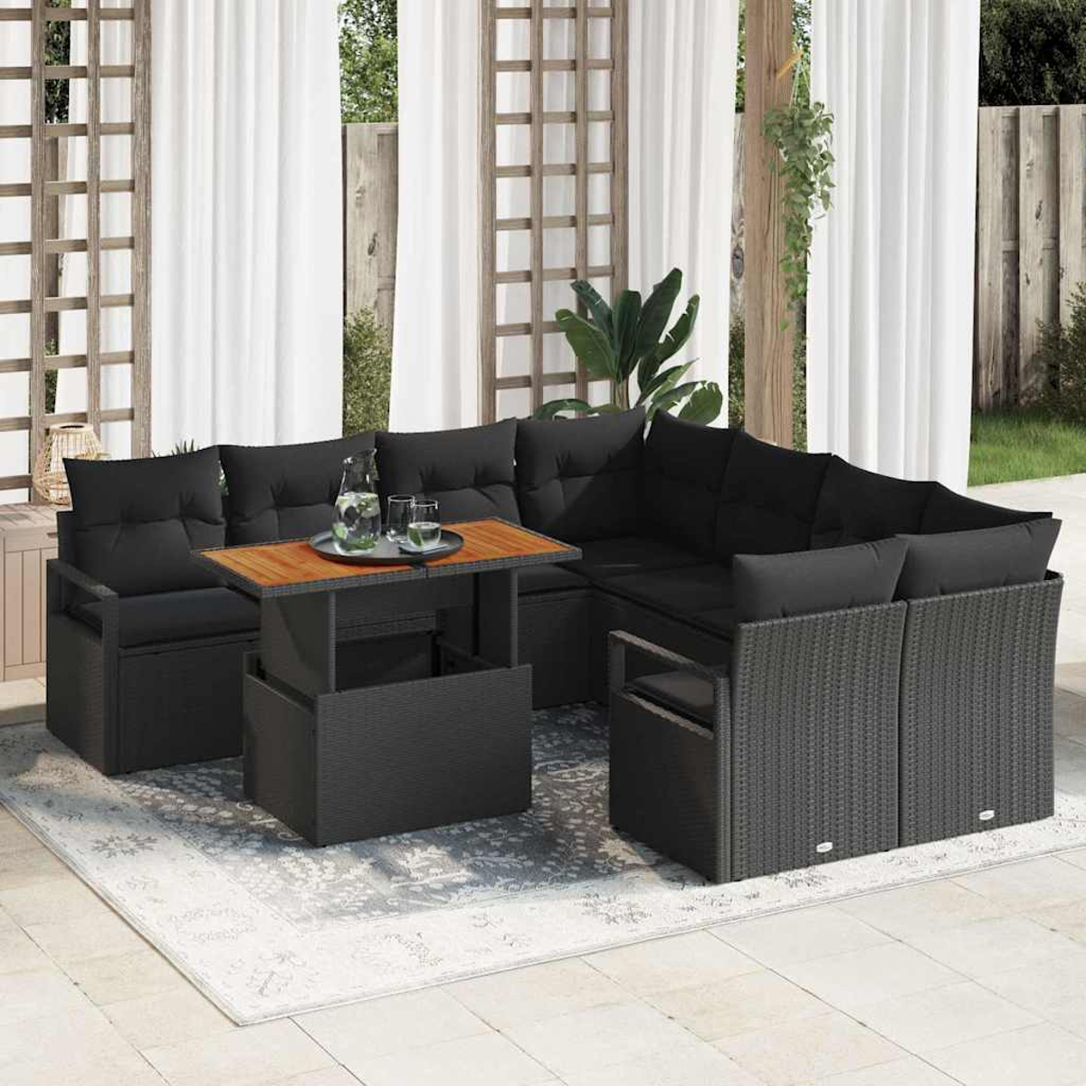 Gartensofa mit schwarzen Kissen. Ein Holztisch trägt ein Tablett mit Gläsern und einem Krug. Weiße Vorhänge im Hintergrund.