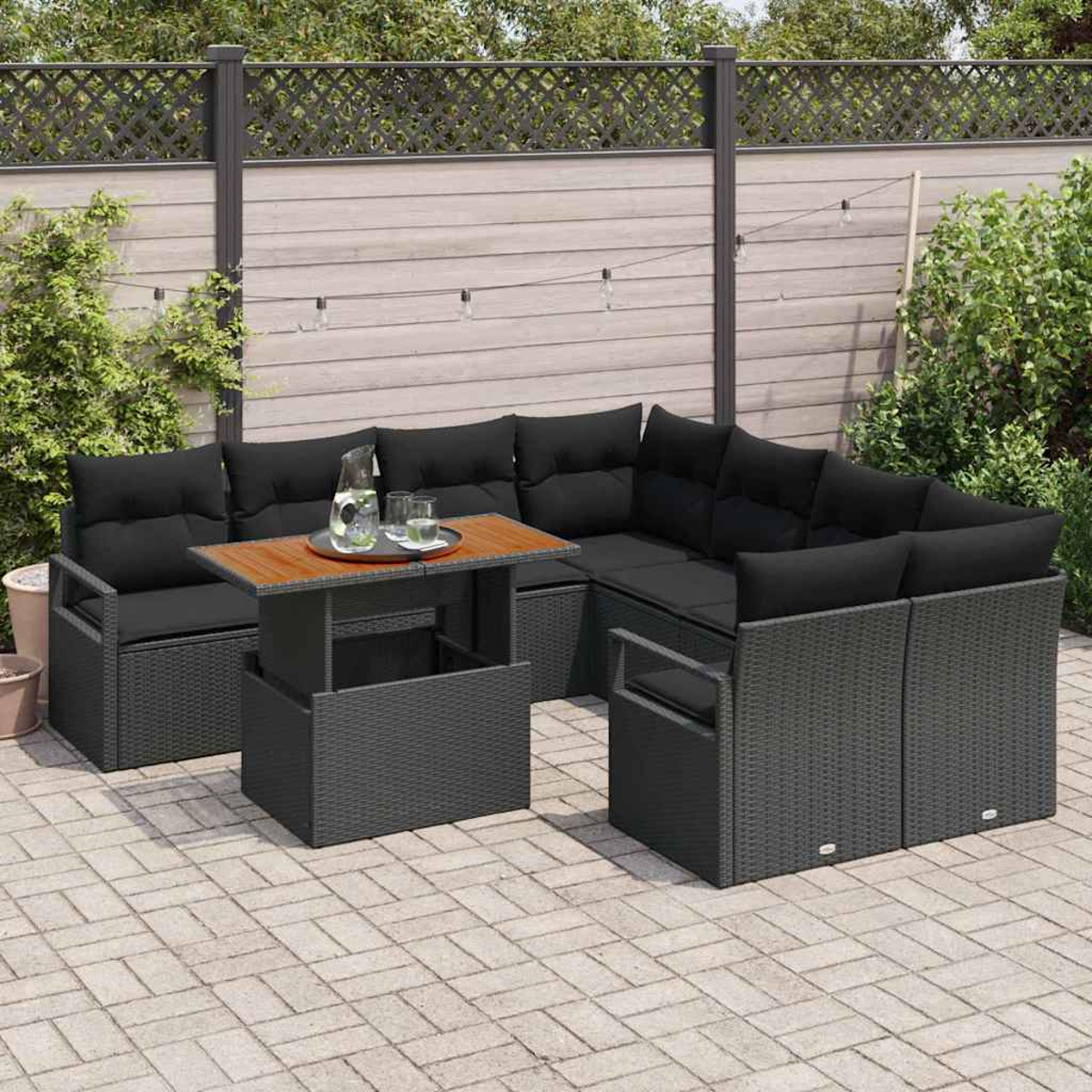 Garten-Sitzgruppe mit schwarzen Kissen, einem Holztisch und einer Kulisse aus Holzzaun und Grün.