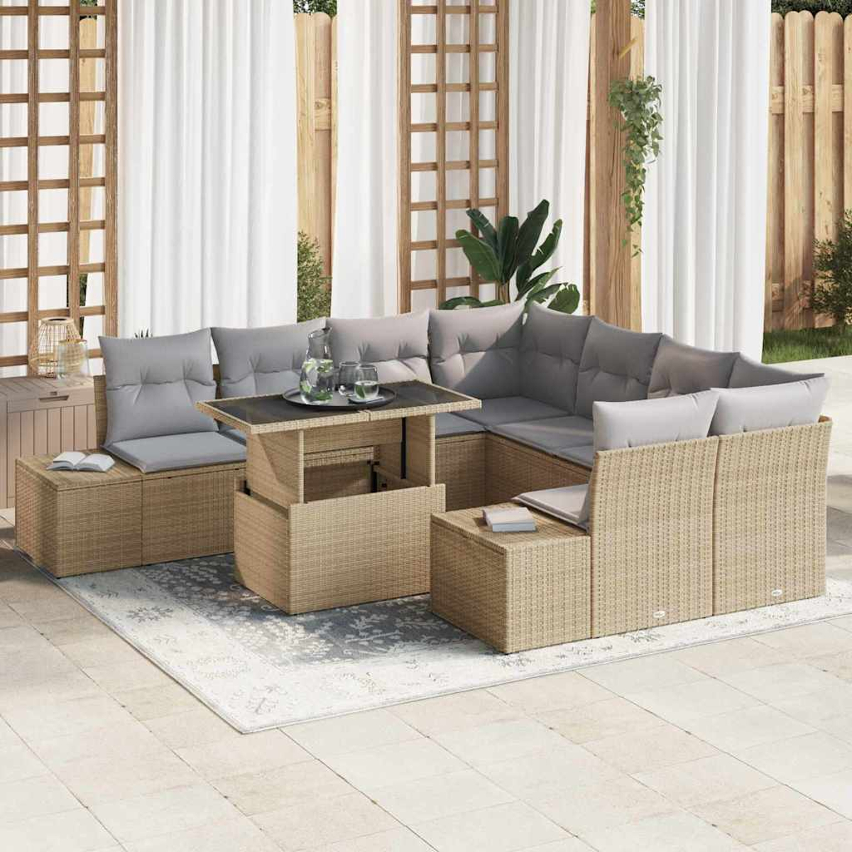 Gartenmöbel-Set aus Korbgeflecht mit grauen Kissen, einem Tisch mit Hubfunktion und einem Teppich. Weiße Vorhänge und Holzzaun im Hintergrund.