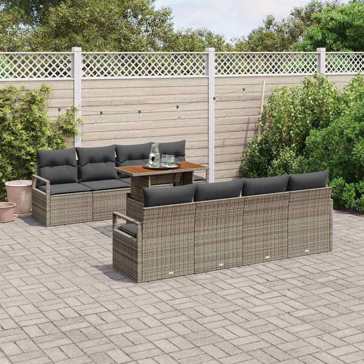 Outdoor-Terrassenset mit grauen Kissen und einem Holztisch. Auf einer Ziegelterrasse, vor einem weißen Zaun und grünen Büschen.