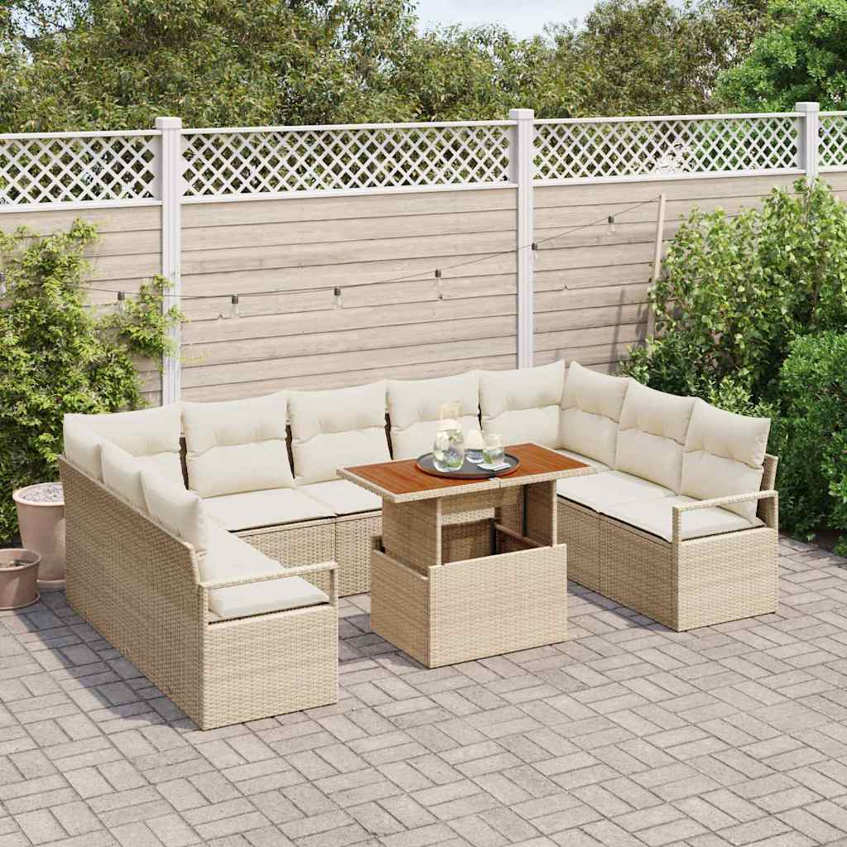 Ein Terrassenset mit beigen Korbmöbeln und cremefarbenen Kissen. Ein Tisch mit Holzplatte steht in der Mitte. Im Hintergrund ist ein weißer Zaun.