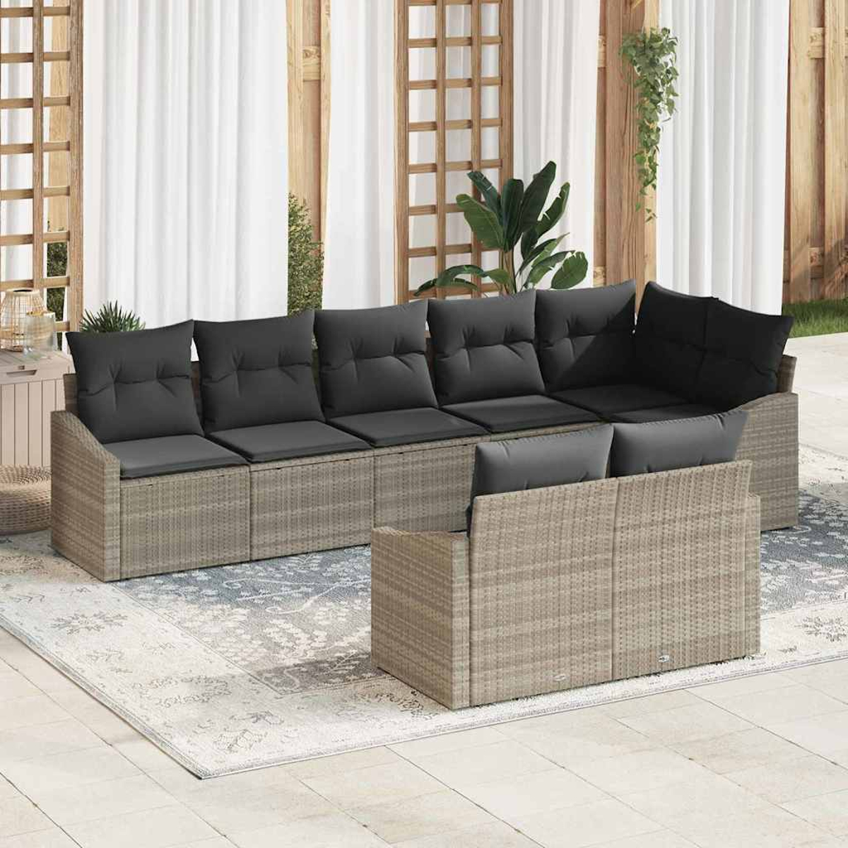 Ein graues Korbsessel-Sofa mit schwarzen Kissen steht auf einem Teppich. Weiße Vorhänge und Holzpaneele sind im Hintergrund.