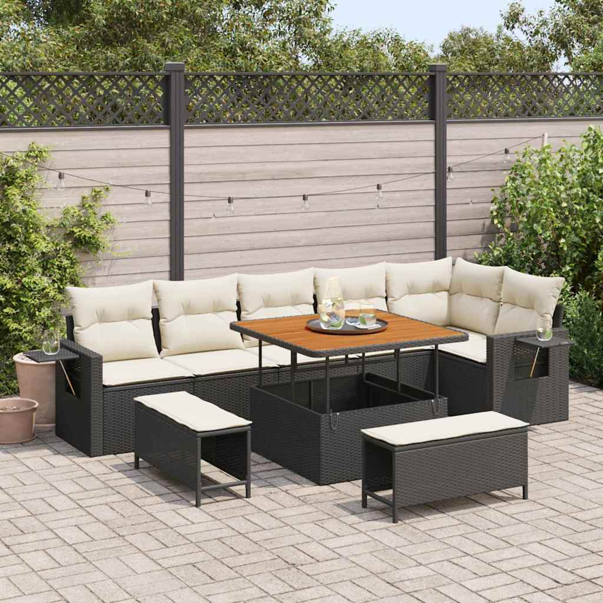 Terrassengarnitur mit Ecksofa, Bänken und einem Tisch mit Hubtisch. Beige Kissen, dunkelgraues Geflecht und ein Holztisch. Gepflasterte Terrasse.