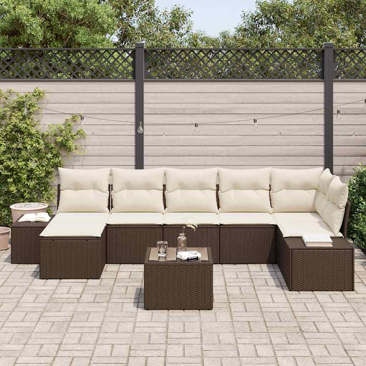 Outdoor-Ecksofa mit cremefarbenen Kissen und einem kleinen Tisch. Eine Backstein-Terrasse mit Holzzaun und Grün im Hintergrund.
