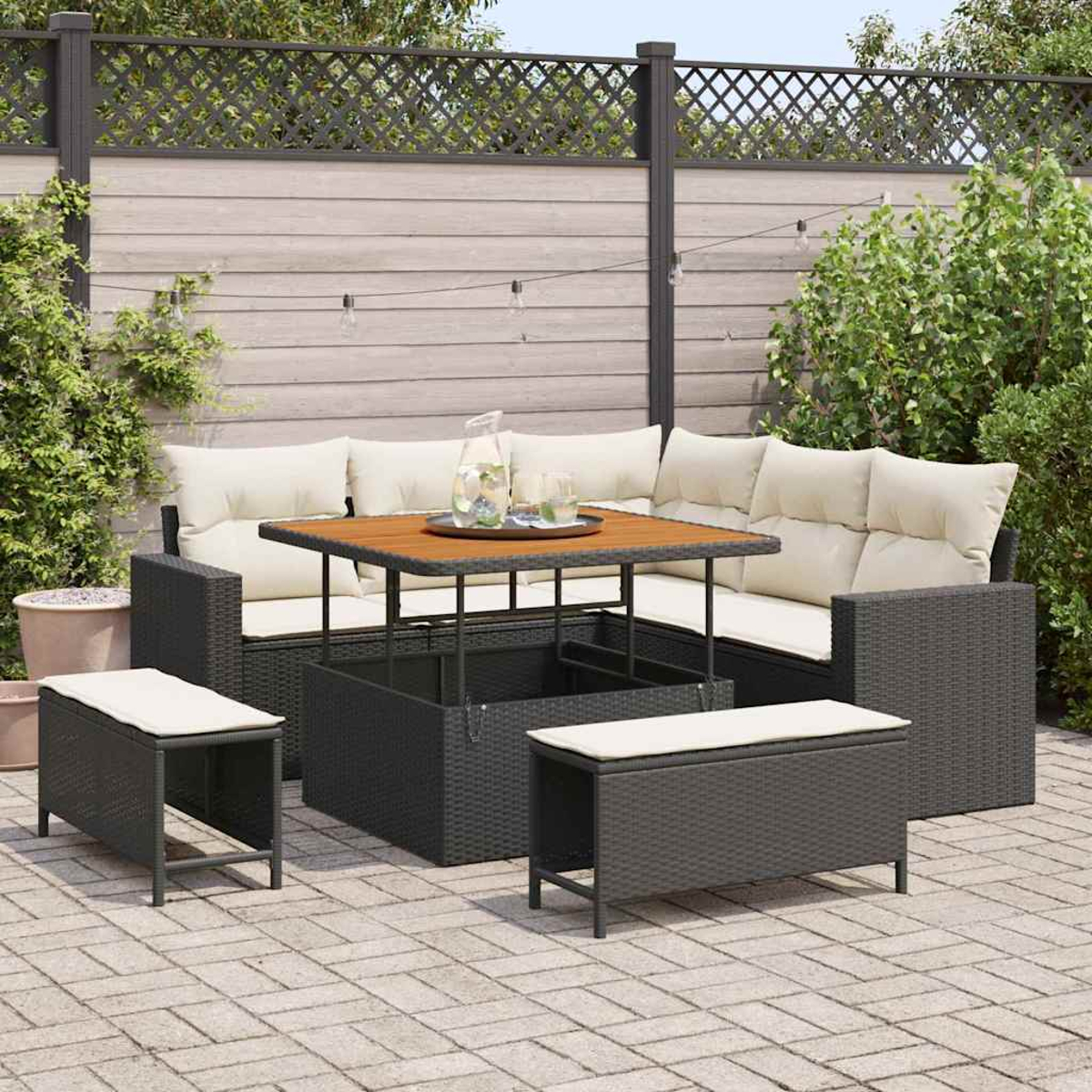 Garten-Sitzgruppe mit Tisch, Bänken und Kissen. Holztisch, Rattanmöbel und Backstein-Terrasse mit Holzzaun im Hintergrund.