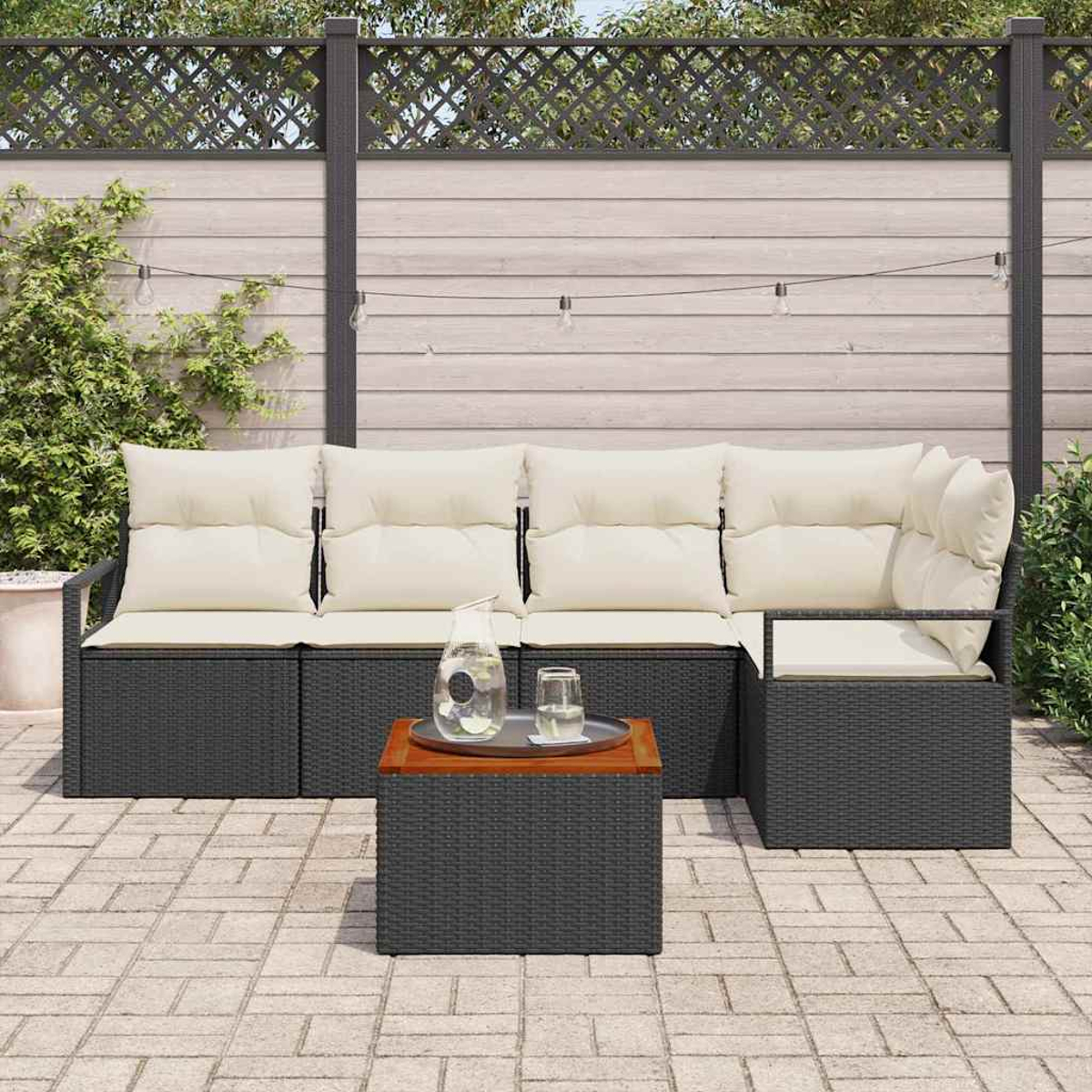 Outdoor-Ecksofa mit beigen Kissen, einem kleinen Tisch mit Getränken und einem Holzzaun im Hintergrund. Ziegelpflaster.