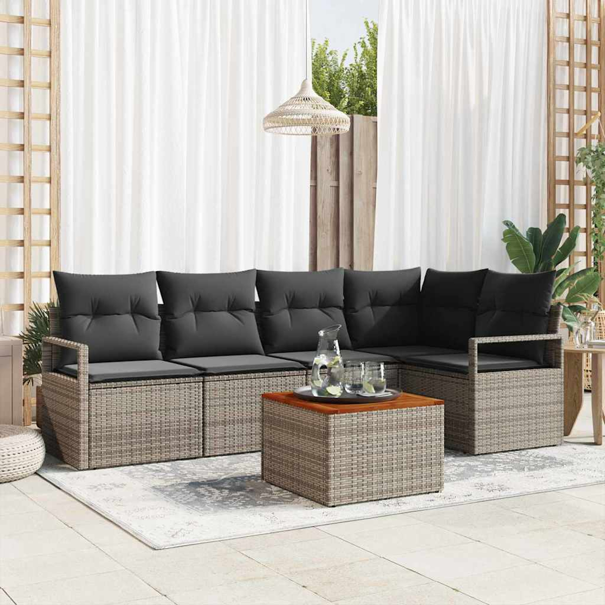 Gartenmöbel-Set mit grauen Kissen, Korbgeflecht-Basis und einem Couchtisch aus Holz. Weiße Vorhänge und eine gewebte Lampe sind im Hintergrund.