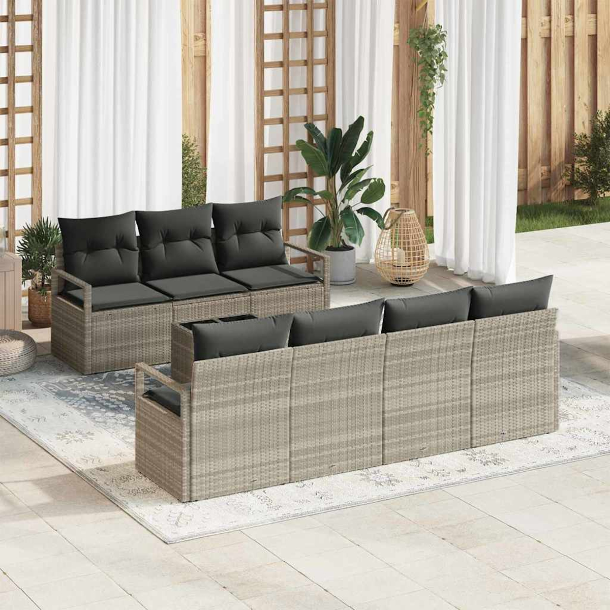 Szene im Freien mit zwei Korbmöbel-Sofas mit grauen Kissen auf einem Teppich. Pflanzen, Vorhänge und ein Spalier im Hintergrund.