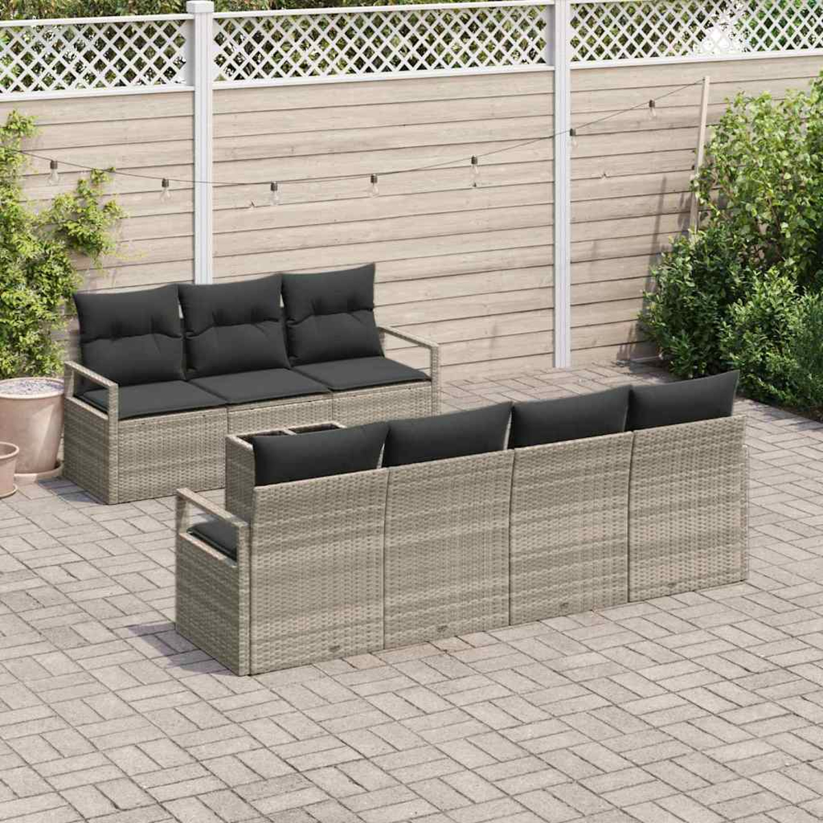 Terrasse im Freien mit zwei Korbmöbeln mit schwarzen Kissen. Im Hintergrund befinden sich ein Holzzaun und Grün. Die Terrasse ist gepflastert.