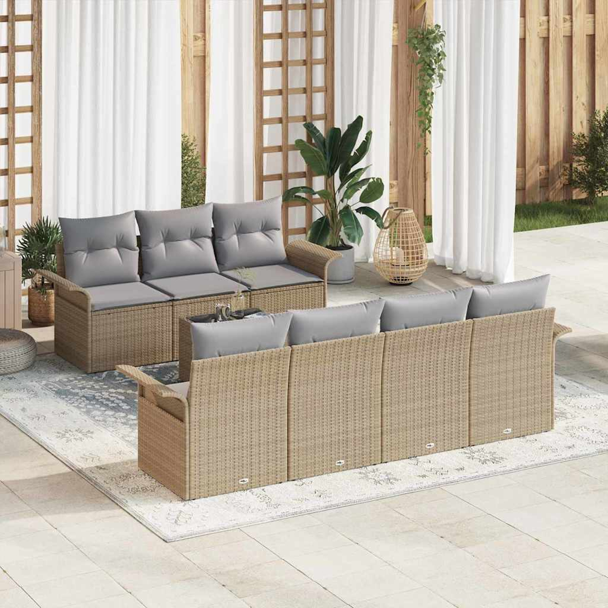 Gartenmöbel-Set. Zwei Korbsitzgruppen mit grauen Kissen auf einem gemusterten Teppich. Weiße Vorhänge und Pflanzen im Hintergrund.