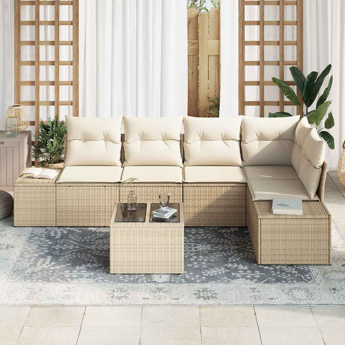Outdoor-Sofa aus Korbgeflecht mit cremefarbenen Kissen und einem kleinen Tisch, auf einem gemusterten Teppich. Pflanzen und Vorhänge im Hintergrund.