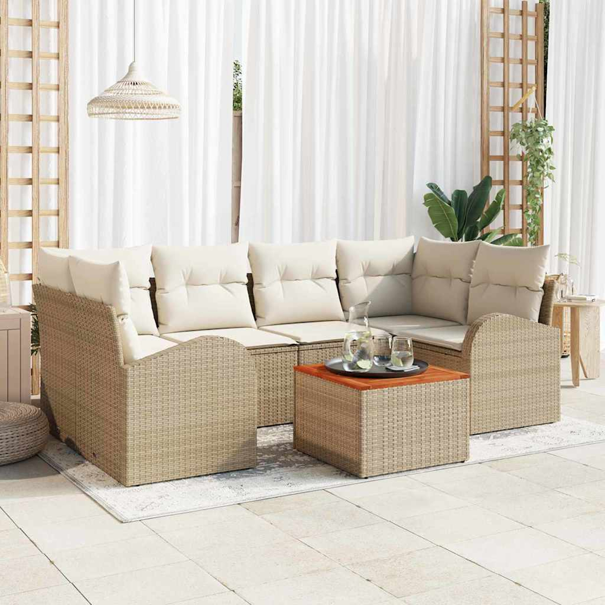 Juego de sofás de ratán para exteriores con cojines blancos y una mesa de café de madera. Cortinas blancas y una lámpara colgante al fondo.