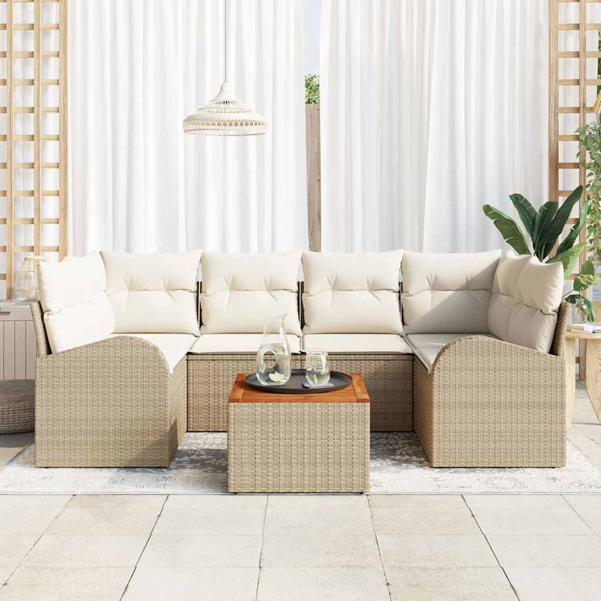 Un sofá seccional de ratán con cojines crema y una mesa de madera. Cortinas blancas y una lámpara colgante en el fondo.