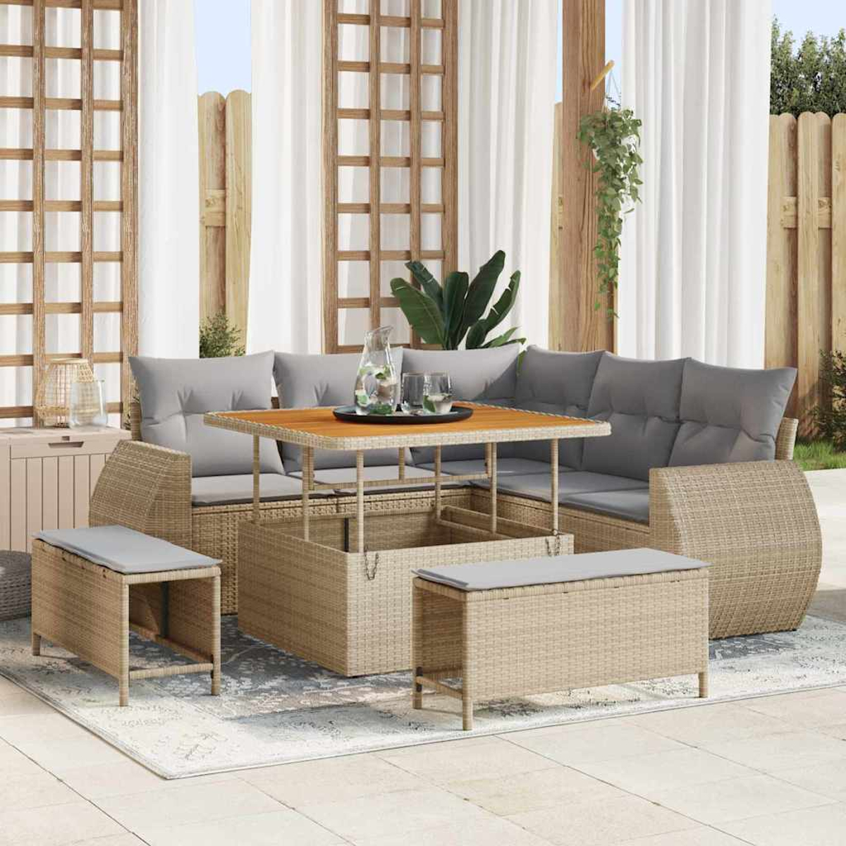 Outdoor-Sofa aus Korbgeflecht mit grauen Kissen, einem Hubtisch und passenden Bänken auf einem Teppich, vor Vorhängen und Holzgitter.