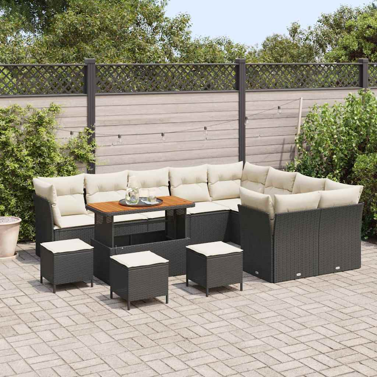 Garten-Terrassenset mit dunkelgrauen Korbmöbeln, beigen Kissen und einem Holztisch. Auf einer Steinterrasse mit einem grauen Zaun im Hintergrund.