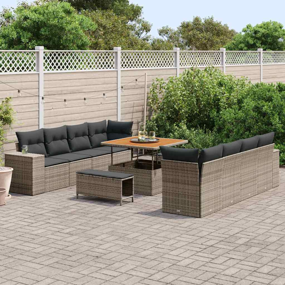 Terrassengarnitur mit grauen Kissen und einem Holztisch. Das Set umfasst ein Sofa, zwei Stühle und eine Bank. Umgeben von Grün.