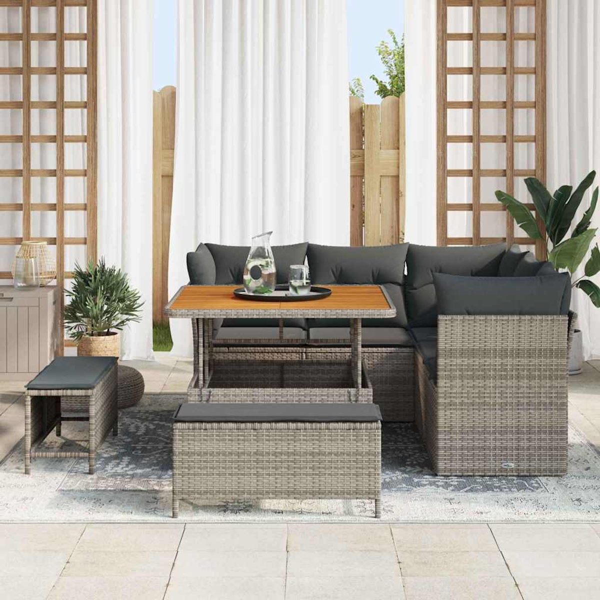Set di sedute da esterno con cuscini grigi e rattan. Include tavolo, panca e divano, su un tappeto vicino a una finestra.
