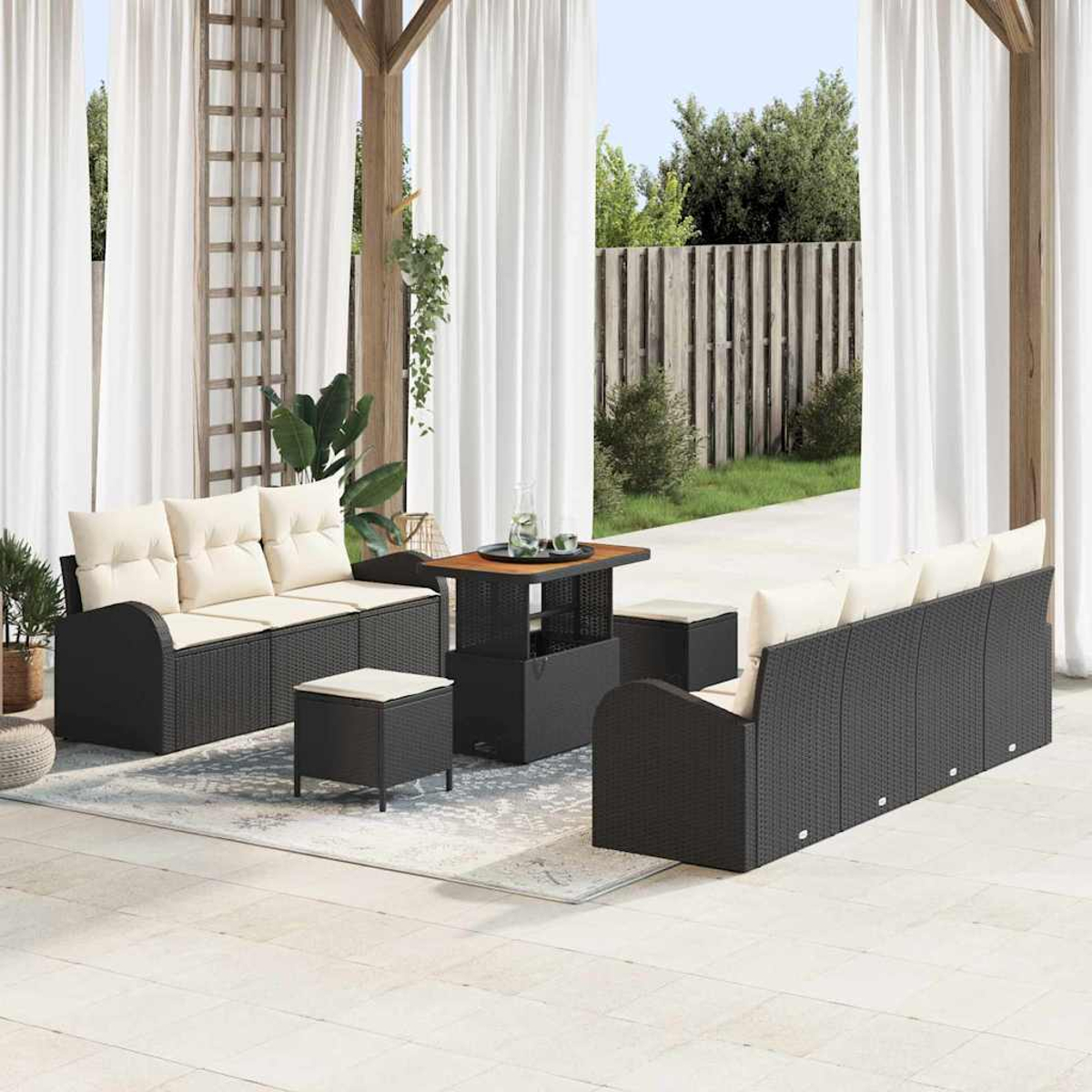 Garten-Sitzgruppe mit schwarzen Korbsesseln, beigen Kissen, Couchtisch und Ottomanen, vor weißen Vorhängen und Garten.
