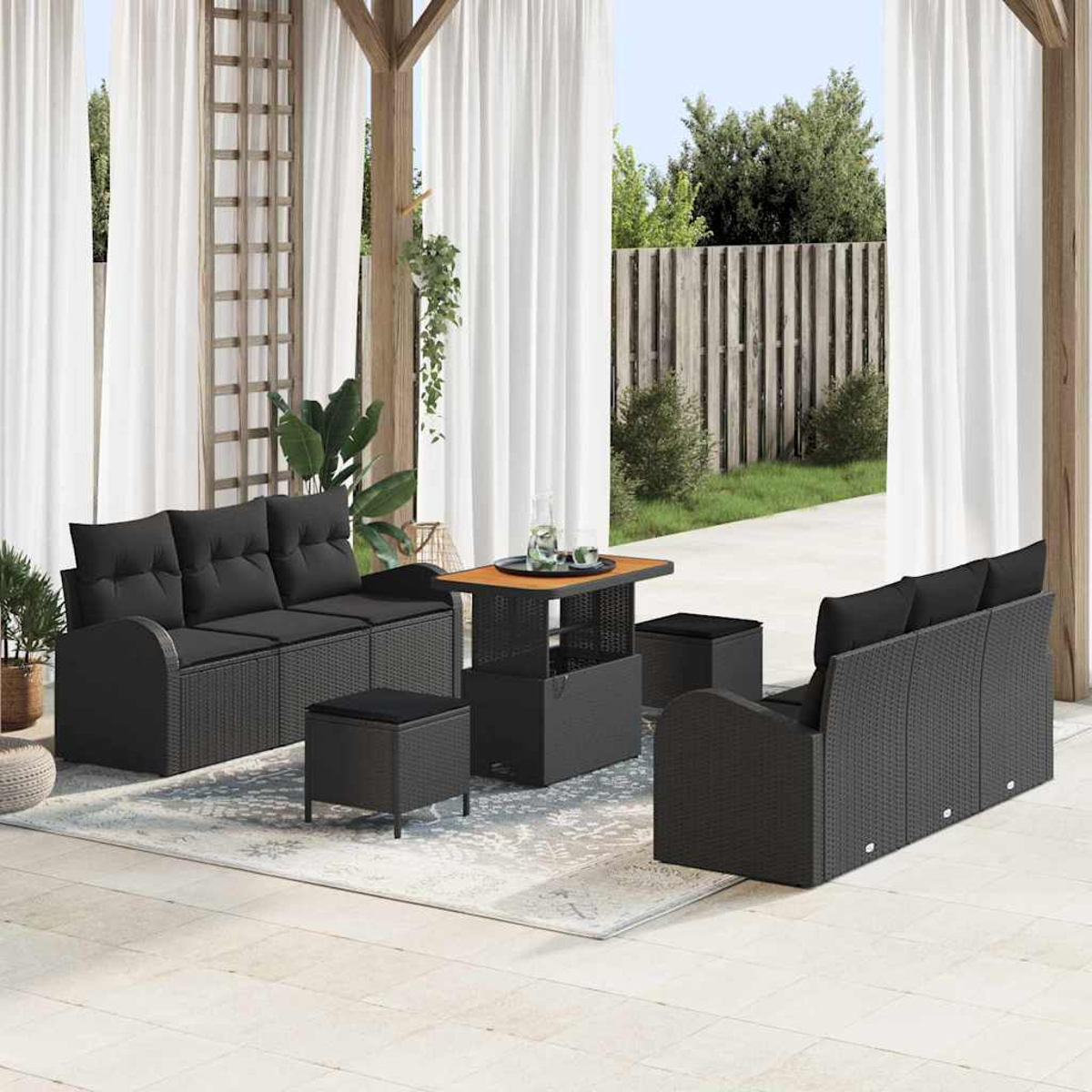 Garten-Terrassenset mit schwarzen Korbsesseln, Ottomanen und einem Tisch. Weiße Vorhänge und Holzpergola rahmen die Aussicht ein.
