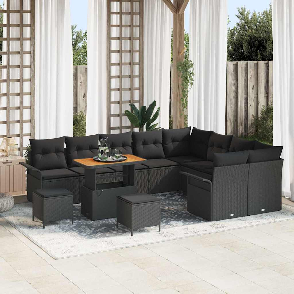 Garten-Sitzgruppe mit schwarzen Kissen und Holztisch auf einem Teppich. Weiße Vorhänge und Holzstrukturen im Hintergrund.