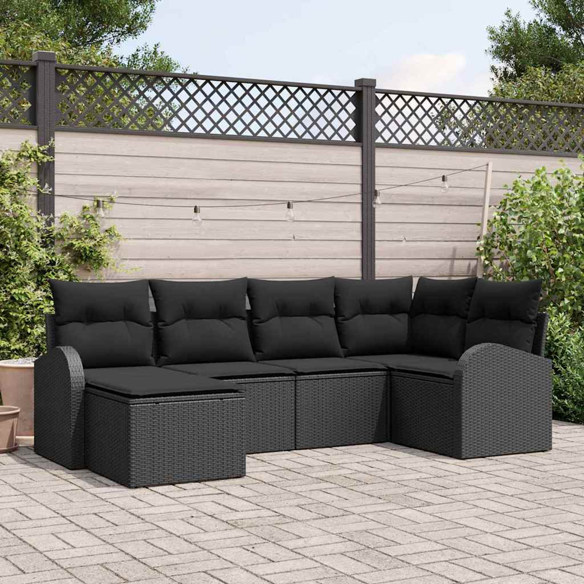 Schwarzes Korbsessel-Sofa auf einer Steinterrasse. Im Hintergrund ein Zaun, Pflanzen und Lichterketten.
