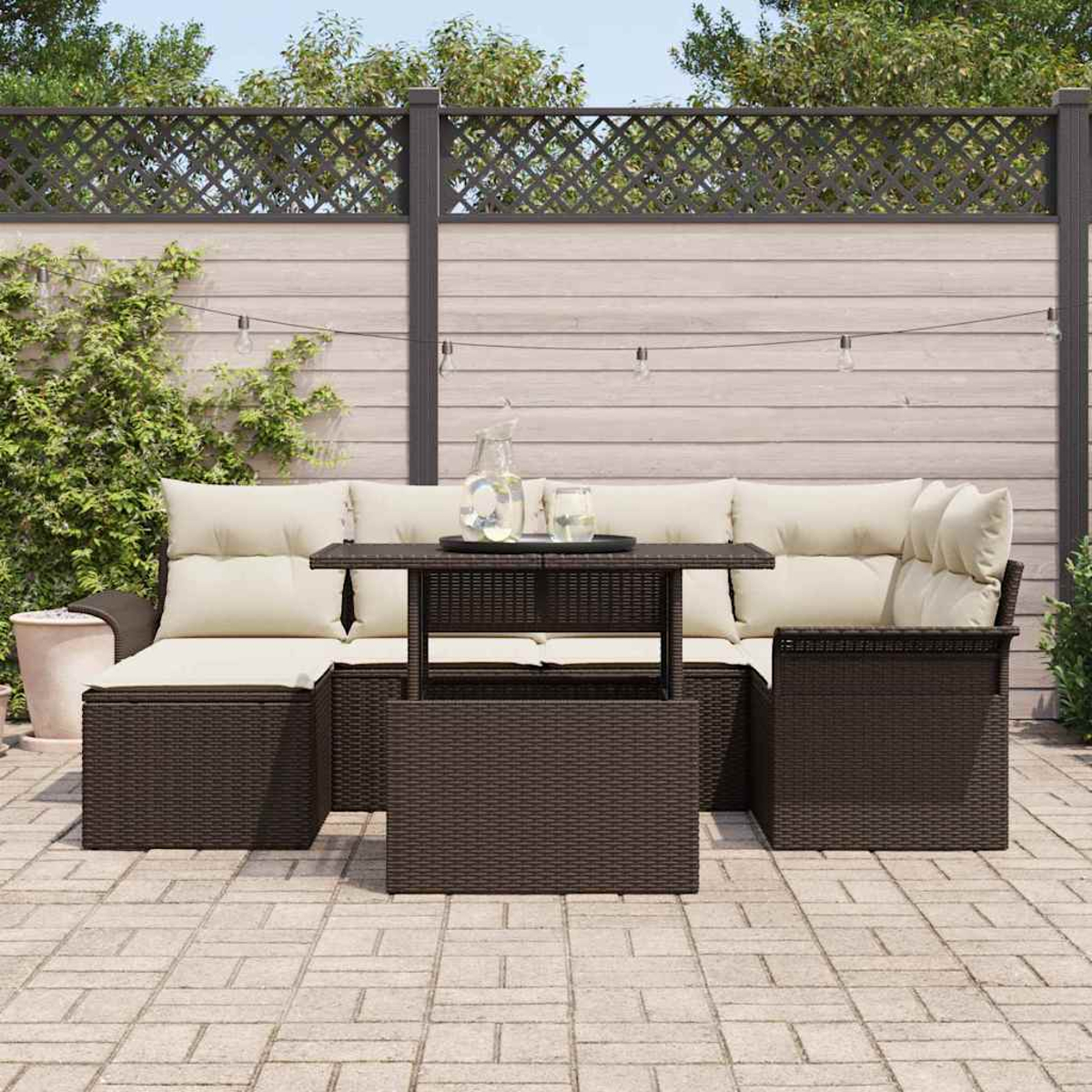 Garten-Terrassenset mit braunen Korbmöbeln, beigen Kissen und einem dunklen Tisch. Im Hintergrund ein Zaun und Grün.