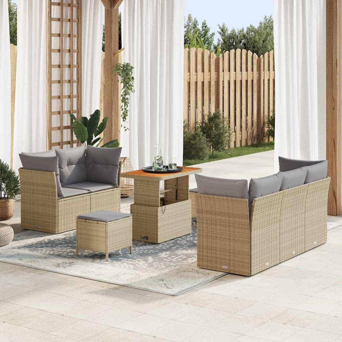 Set patio esterno. Mobili in vimini beige con cuscini grigi. Include divano, sedie, pouf e tavolo, su un tappeto fantasia.