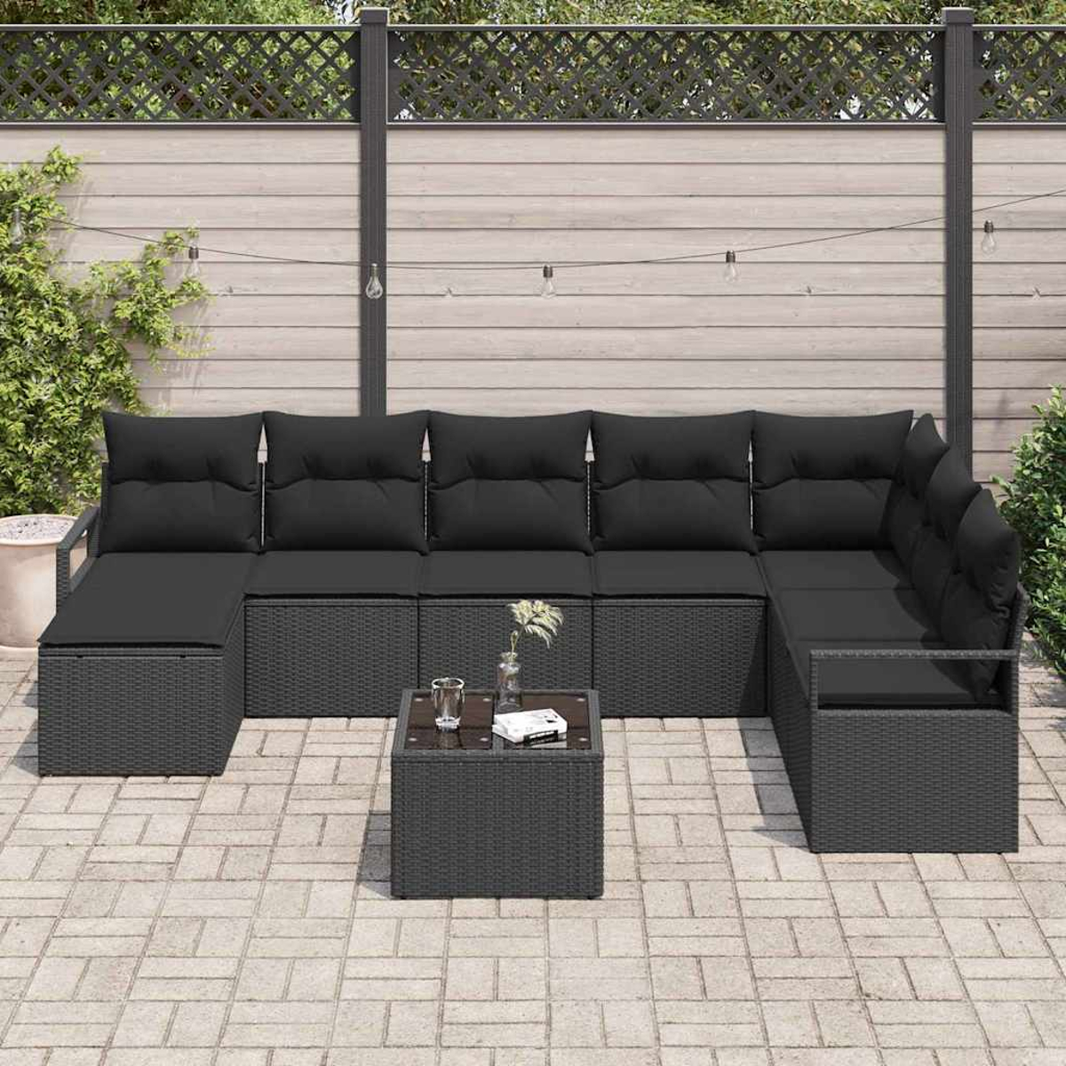 Ein schwarzes Outdoor-Ecksofa mit Kissen und ein passender Couchtisch auf einer gepflasterten Terrasse. Im Hintergrund befindet sich ein Holzzaun.