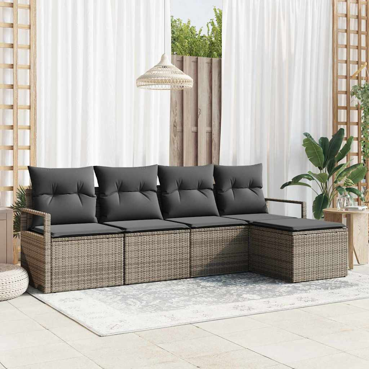 Geflochtenes Outdoor-Ecksofa mit grauen Kissen auf einem gemusterten Teppich, in der Nähe von weißen Vorhängen und Pflanzen. Eine Hängelampe ist ebenfalls sichtbar.