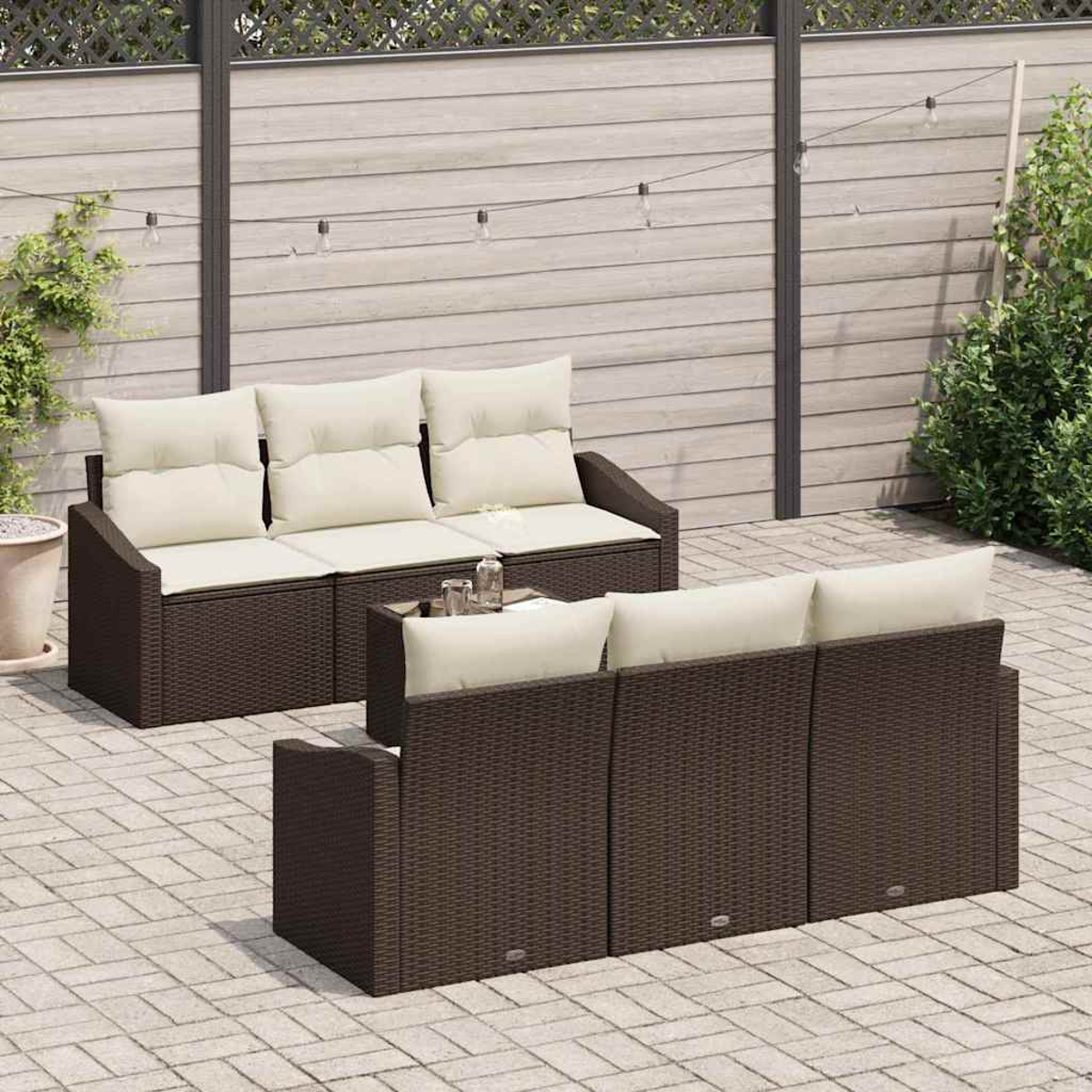 Outdoor-Korbsessel-Set mit cremefarbenen Kissen. Zwischen den Sofas steht ein kleiner Glastisch. Im Hintergrund ein Holzzaun und Grün.